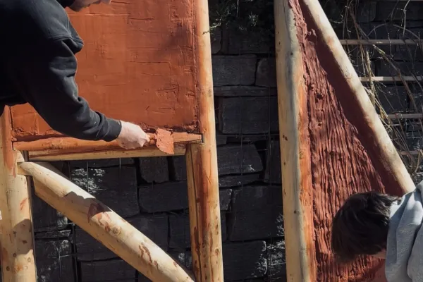ZweiStudierende füllen einen Holzrahmen mit rot eingefärbtem Lehm