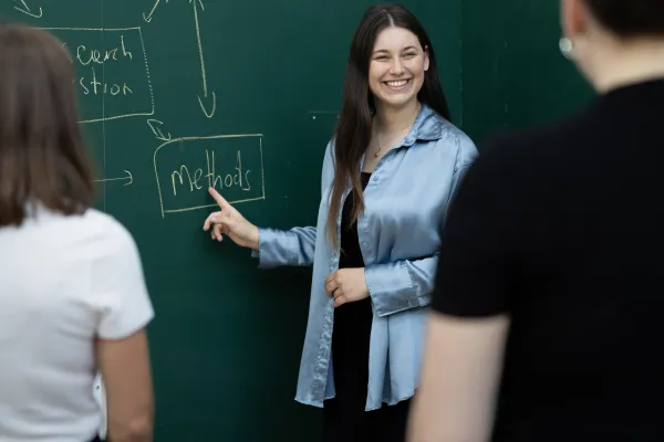 Studierende präsentieren ein Forschungskonzept an der Tafel und diskutieren Methoden an der Universität Liechtenstein.