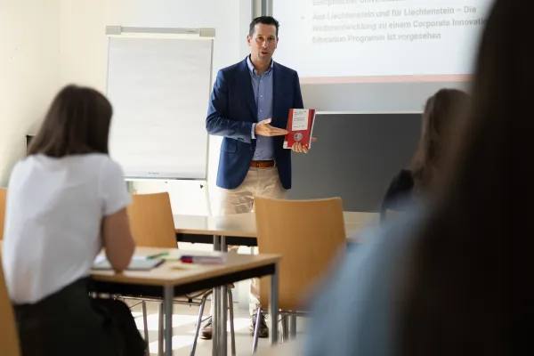 Dozent der Universität Liechtenstein präsentiert ein Fachbuch zum Thema Innovation vor Studierenden im Seminarraum.