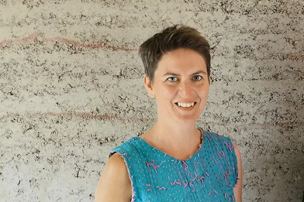 Frau mit blauem Shirt vor einer Stampflehmwand