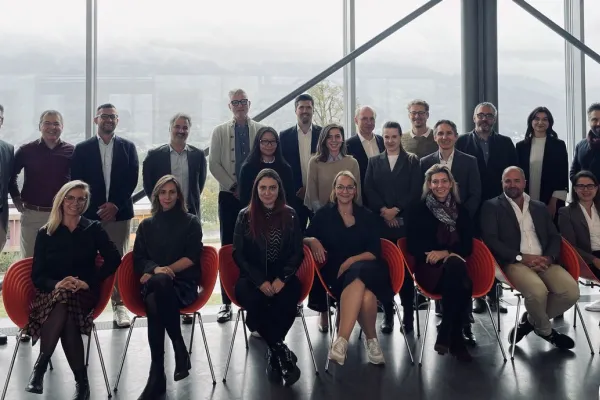 Gruppenfoto von Teilnehmenden der MiCAR Expert Roundtable Series an der Universität Liechtenstein. Die Personen stehen und sitzen in zwei Reihen vor einer großen Fensterfront mit Blick auf eine bergige Landschaft.