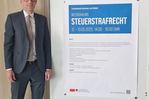 Ein Mann in Anzug steht neben einem Plakat, das den Intensivkurs „Steuerstrafrecht“ der Universität Liechtenstein ankündigt. Das Plakat enthält Informationen zu Datum, Uhrzeit und Inhalten des Kurses.