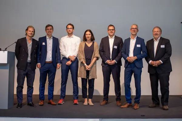 Eine Gruppe von sieben Personen steht auf einer Bühne beim 8. Liechtenstein Workshop of Sustainable Finance an der Universität Liechtenstein. Sie tragen formelle Kleidung und lächeln in die Kamera.