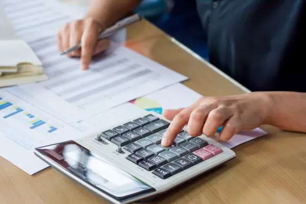 Person sitzt am Tisch mit Taschenrechner und Papier und rechnet