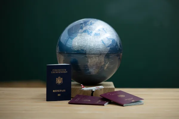 Globus mit Reisepässen aus Liechtenstein und EU sowie Modellflugzeug auf Tisch.