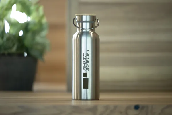 Edelstahl-Trinkflasche mit Logo der Universität Liechtenstein vor Pflanze.