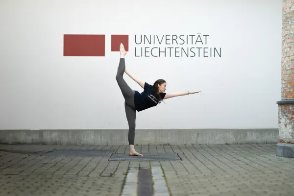 Woman Practising Yoga in Front of the University of Liechtenstein Logo