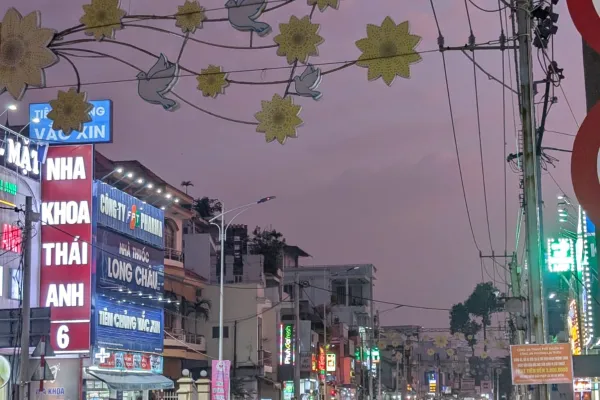 Belebte Straße bei Dämmerung mit vielen Motorrollern, leuchtenden Werbeschildern und dekorativen Lichtern über der Fahrbahn.