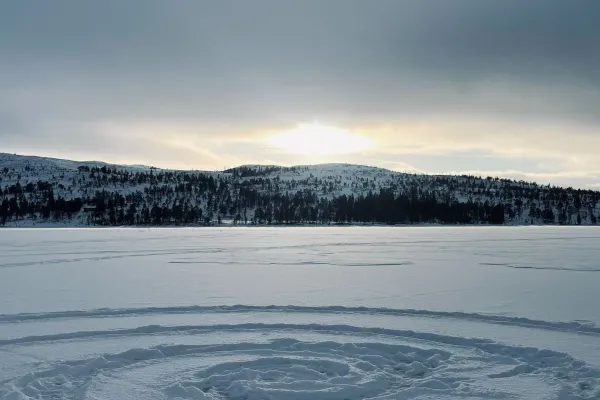 Spiralförmige Spur im Schnee auf gefrorenem See vor Hügeln.