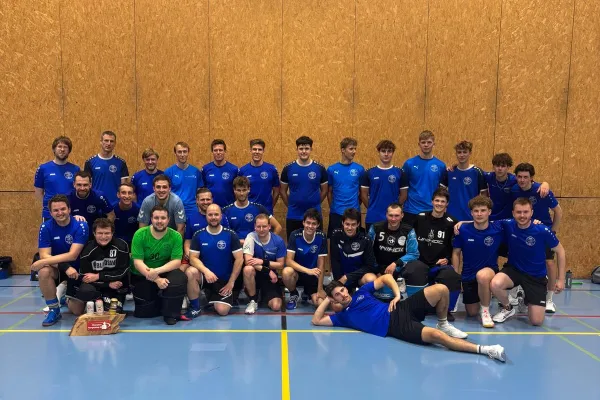 Group photo of a handball team wearing blue jerseys in a sports hall.