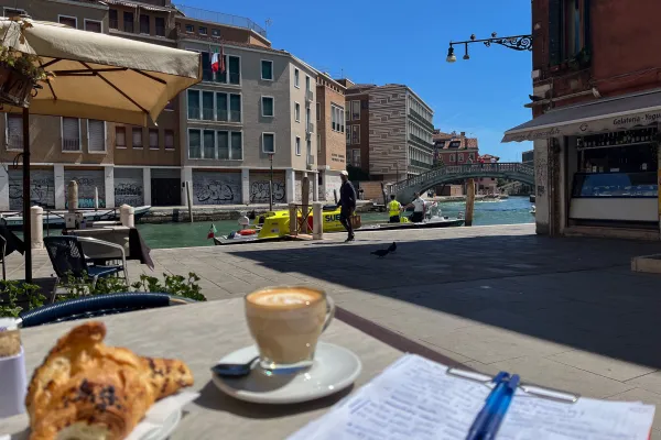 Coffee, croissant and notes on a table by a canal in Venice.