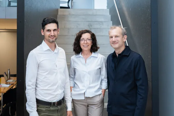 Zwei Männer und eine Frau stehen vor einer Treppe und blicken in die Kamera