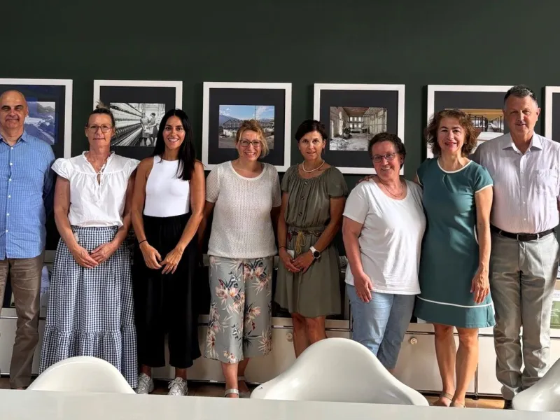 Eine Gruppe von acht Personen steht lächelnd vor einer Wand mit gerahmten Bildern. Sie befinden sich in einem Besprechungsraum der Universität Liechtenstein.